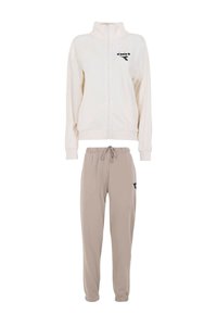 Giacca crema con cerniera e colletto alto, con logo nero; abbinata a pantaloni jogger beige con vita elastica e accento nero.