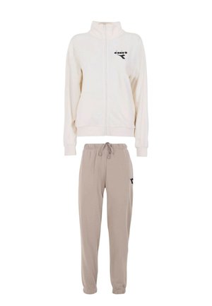 Giacca crema con cerniera e colletto alto, con logo nero; abbinata a pantaloni jogger beige con vita elastica e accento nero.
