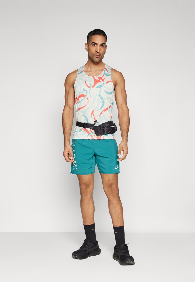 Camiseta sin mangas atlética con un patrón abstracto multicolor, combinada con pantalones cortos azul verdoso que tienen un patrón lateral. Riñonera negra y zapatillas de correr.