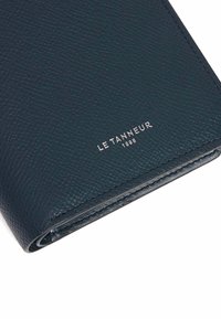 Dunkelblaues, strukturiertes Lederportemonnaie mit sichtbaren Nähten und einem silbernen, geprägten Logo. Kompakte Bauweise mit glatten Kanten.