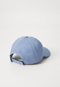 Boné de basebol azul-claro em algodão com uma viseira curvada, tirante ajustável na parte de trás e detalhe em relevo "EST 1922". Textura suave.