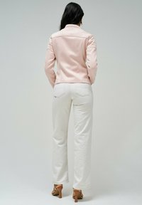 Svetlo roza prilegajoča jakna s prešitim detajlom na ramenih, v kombinaciji s kremnimi širokimi hlačami in rjavimi petami. Gladek material, sodoben silhuet.