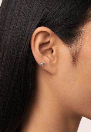Orecchino a stella in oro con pietre di turchese disposte in un motivo floreale, messo in risalto da una vista ravvicinata dell'orecchio e dei capelli di una persona.