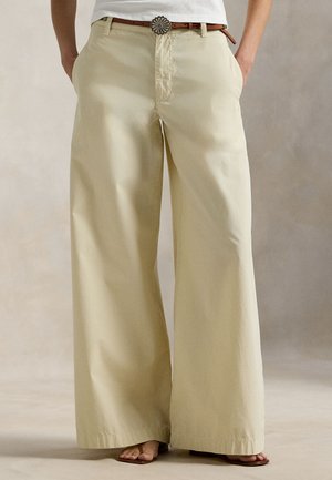 Lysebeige bukser med brede ben lavet af et glat stof, med forlommer og et brunt bælte med en dekorativ spænde.