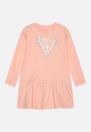 Langærmet ferskenfarvet kjole med flæsekant og blomsterdetaljeret Guess-logo med en trekant og et spørgsmålstegn på brystet.
