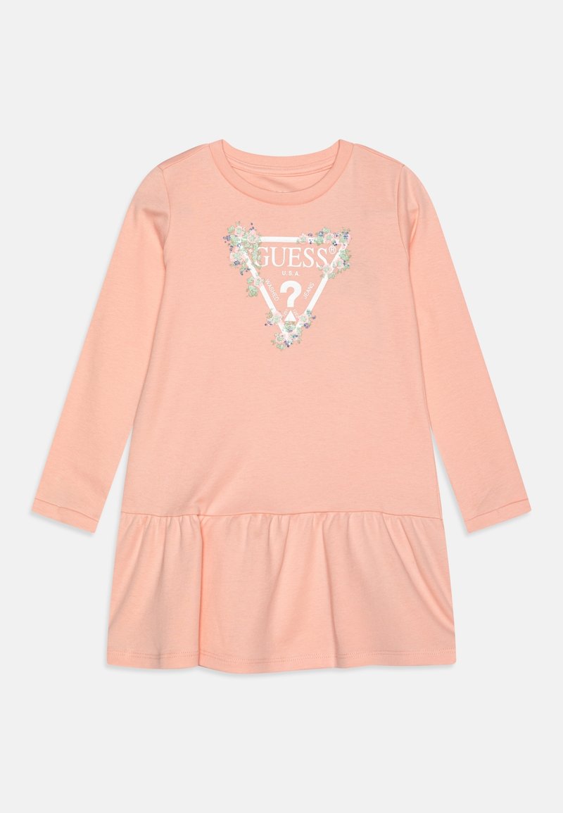 Robe manches longues couleur pêche avec ourlet à volants et logo Guess orné de fleurs, présentant un triangle et un point d’interrogation sur la poitrine.