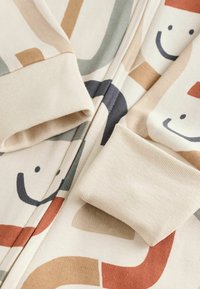 Tissu doux couleur crème avec des poignets côtelés et un motif de formes abstraites multicolores et de visages souriants.