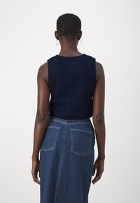 Ναυτικό αμάνικο τοπ συνδυασμένο με ψηλόμεση τζιν φούστα που διαθέτει δύο πίσω τσέπες και ίσια γραμμή. Λείες υφές και καθαρές γραμμές.