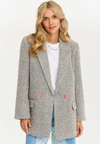 Sako s houndstooth vzorem v mnohobarevném tkaní, se dvěma růžovými knoflíky, s klopovými límci a volným střihem. Texturovaná látka a boční kapsy.