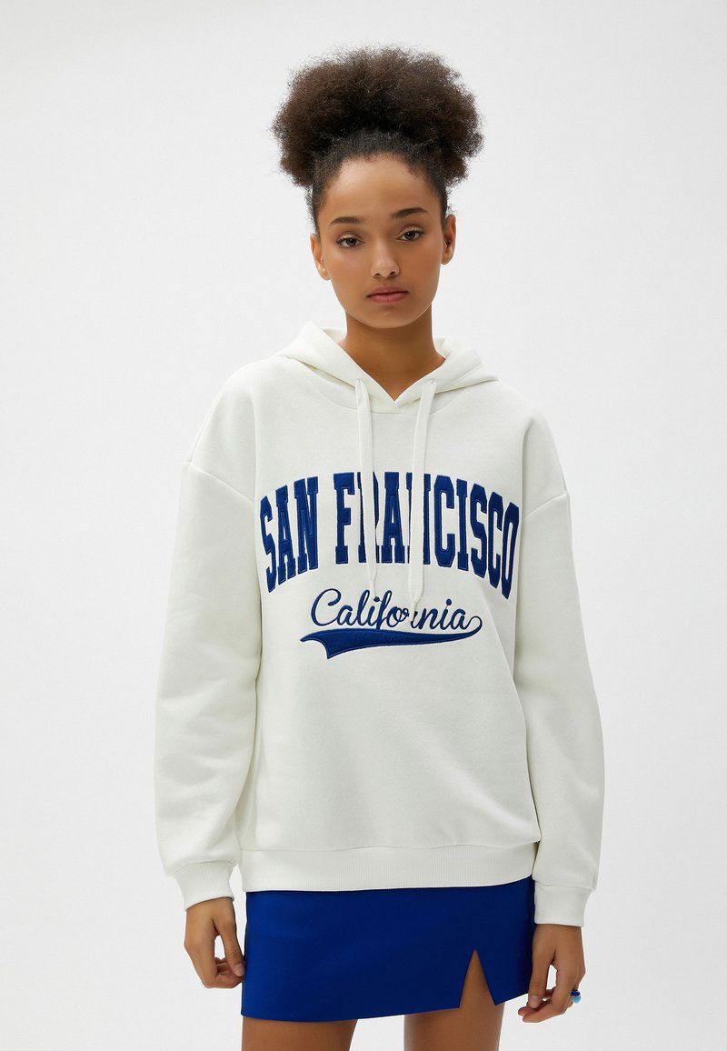 Biała bluza z kapturem z napisem "SAN FRANCISCO" oraz "Kalifornia" w niebieskim kolorze. Charakteryzuje się luźnym krojem oraz ściągaczem na dole.