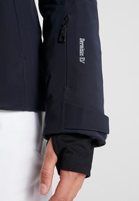 Námořnická nepromokavá bunda s kapsou na zip na rukávu, manžetou s otvorem na palec a detaily s logem; hladká textura s přiléhavým designem a nastavitelnou manžetou.