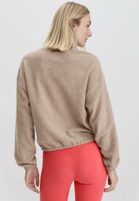 Beige Fleece-Sweatshirt mit cropped Design, elastischem Saum und Ballonärmeln, kombiniert mit leuchtend korallenfarbenen Leggings. Die weiche Textur ist sichtbar.