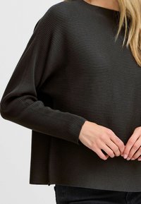 Donkergroene geribbelde trui met een ronde halslijn, verlaagde schouders en een relaxte pasvorm, gemaakt van een zachte en gestructureerde stof.