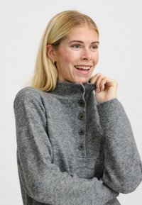 Pulover gri tricotat cu guler înalt, având un sistem de închidere cu nasturi și manșete cu textură canelată, prezentat cu o textură subtilă și un aspect moale.