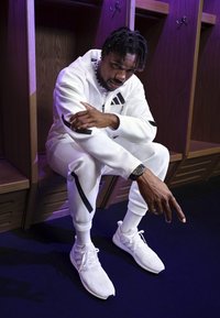 Vit idrottsdräkt med svarta ränder, tillsammans med vita sneakers. Texturerad tyg och reflexdetaljer ökar det visuella intresset.