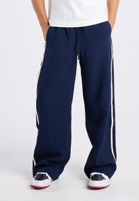 Navy blue pants with white side stripes, made of soft fabric; loose fit with an elastic waistband and visible drawstring.