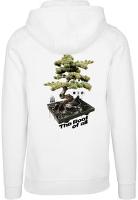 Sudadera blanca con un gráfico detallado de un bonsái con raíces sobre un tocadiscos negro, el texto debajo dice "La raíz de todo."