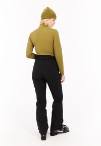 Olijfgroene longsleeve top met hoge kraag, gecombineerd met zwarte skibroek met een gestructureerde tailleband. Zwarte skibotten maken de outfit compleet.