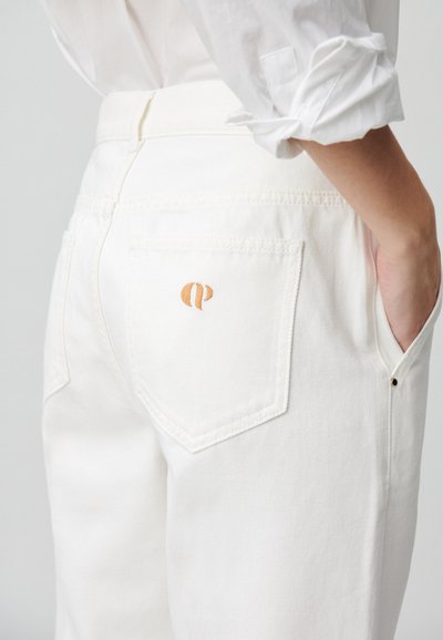 I pantaloni in denim bianco presentano una tasca posteriore con un logo ricamato in arancione. Il tessuto ha una leggera texture e una vestibilità su misura, con una cucitura visibile.