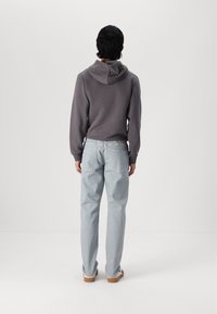 Grå hettegenser med hette, kombinert med lyseblå denim jeans. Silhuetten er avslappet, med et enkelt design som har baklommer.