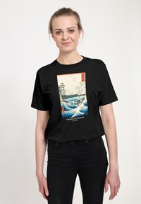 Černé tričko s krátkým rukávem s výraznou grafikou vln a hor. Pod motivem je text „ASHMOLEAN MUSEUM OXFORD".