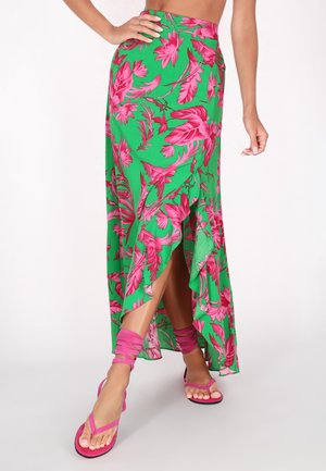 Gonna maxi floreale verde con fantasie rosa, orlo arricciato, spacco alto, abbinata a sandali rosa con cinturini che si avvolgono attorno alle gambe.