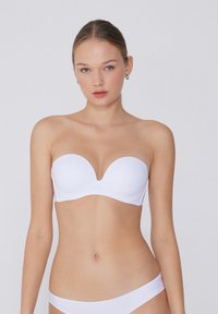 Bílá podprsenka bez ramínek s hlubokým V výstřihem, hladkou texturou a tvarovanými košíčky. Minimalistické kovové prvky a bezšvové okraje pro čistý vzhled.