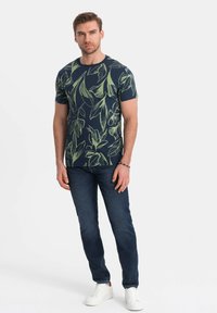 Marine T-shirt met groen bladerenpatroon, korte mouwen, ronde hals. Gecombineerd met donkere jeans en witte sneakers. Soepele stofstructuur.