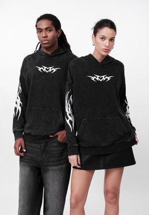 Sorte hættetrøjer med hvide flamme-motiver på ærmer og bryst, med en frontlomme. Modellen bærer denim og en faux lædernederdel.