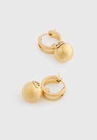 Arany karika fülbevalók sima, kerek medálokkal és apró díszített gravírozásokkal egy sima fehér háttéren.