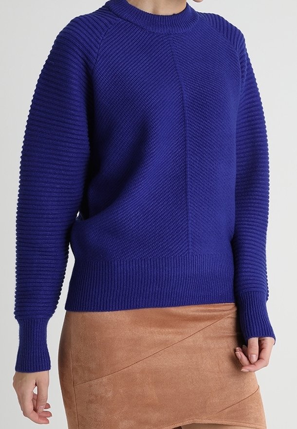 Pull en tricot violet avec une texture côtelée, un col rond et des manches longues. Associé à une jupe en daim beige avec des coutures diagonales.