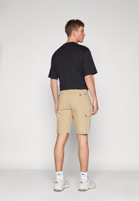 Pantaloni cargo beige con tasche, abbinati a una maglietta nera a maniche corte. I pantaloni hanno una vestibilità comoda e una texture liscia.