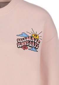 Hellrosa Sweatshirt mit einem grafischen Druck, der den Text "Feier sonnige Tage", eine Sonne, Wolken und eine Blume in lebhaften Farben zeigt.