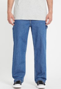 Pantalones cargo de mezclilla en azul medio, con bolsillos laterales, un corte relajado y costuras contrastadas. Combinados con zapatillas negras.
