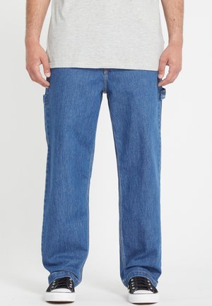 Denim cargo pants in medium blue, featuring side pockets, a relaxed fit, and contrasted stitching. Paired with black sneakers.