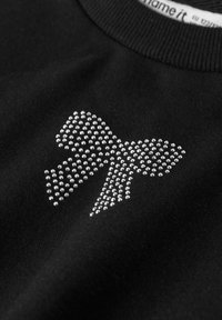 Juoda medžiaga su balta kalnų krištolo kaspino dizainu prie apykaklės ir iš dalies matomu drabužių etikete.