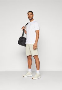 Vit kortärmad skjorta, ljusbeige shorts och beige träningsskor. En svart sportväska med ett nätfack. Enkel design, avslappnad stil.