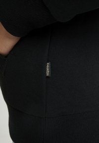 Felpa nera con texture morbida, polsini a costine e un piccolo logo "Superdry" ricamato sulla cucitura laterale.