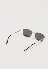 Gafas de sol con montura dorada, lentes oscuras y extremos de varilla con patrón de carey, descansando sobre un fondo claro.