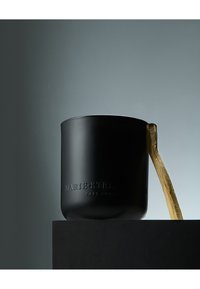 Tazza in ceramica nera opaca con testo in rilievo e manico curvo in legno su una superficie scura, contro uno sfondo grigio tenue.