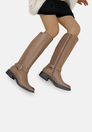Bottes marron jusqu'au genou avec une finition lisse, dotées d'une fermeture éclair sur le côté et d'un accent de boucle. Texture mate avec un petit talon carré.