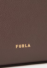 Brown textured leather bag featuring embossed "FURLA" logo in gold. Smooth edges and subtle grain detail enhance its design.