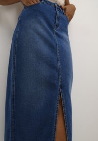 Falda maxi de mezclilla con una abertura lateral, presenta una cintura alta, color azul y costuras clásicas a lo largo de las costuras.
