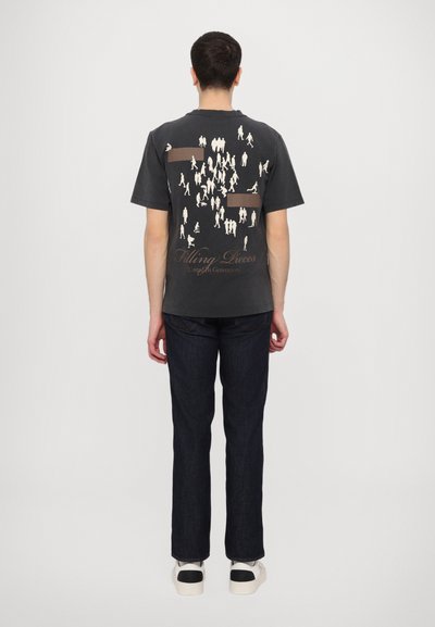 T-shirt à manches courtes gris foncé avec un graphique de silhouettes blanches et le texte "Filling Pieces" au dos. Associé à un jean en denim foncé.