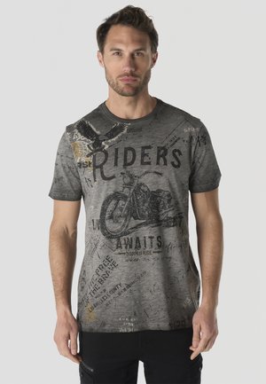 Hombre que lleva una camiseta gris con gráficos de motocicleta y águila y la palabra Riders en texto negro en la parte delantera.