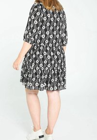 Robe noire à motif floral blanc, longueur au genou, manches courtes bouffantes, ourlet à volants. Portée avec des baskets blanches. Texture de tissu lisse.