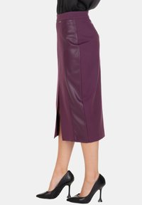 Gonna midi viola con corpo testurizzato e pannelli laterali in ecopelle, con un'alta spacco per facilità di movimento. Abbinata a tacchi neri.