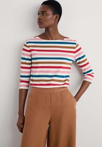 Gestreiftes Langarmshirt mit roten, pinken, braunen und blauen Streifen, kombiniert mit beigen weiten Hosen. Das Shirt hat einen Boot-Ausschnitt und Dreiviertelärmel.