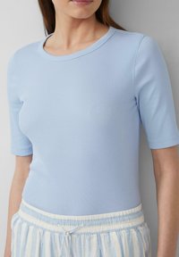 Top corto a maniche corte di un blu chiaro a coste con scollatura rotonda, abbinato a pantaloni corti a righe chiare con laccetto in vita.