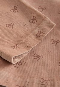 Tessuto a coste beige con una superficie testurizzata, che presenta un motivo ripetuto di fiocchi marroni e una distintiva rifinitura delle cuciture.